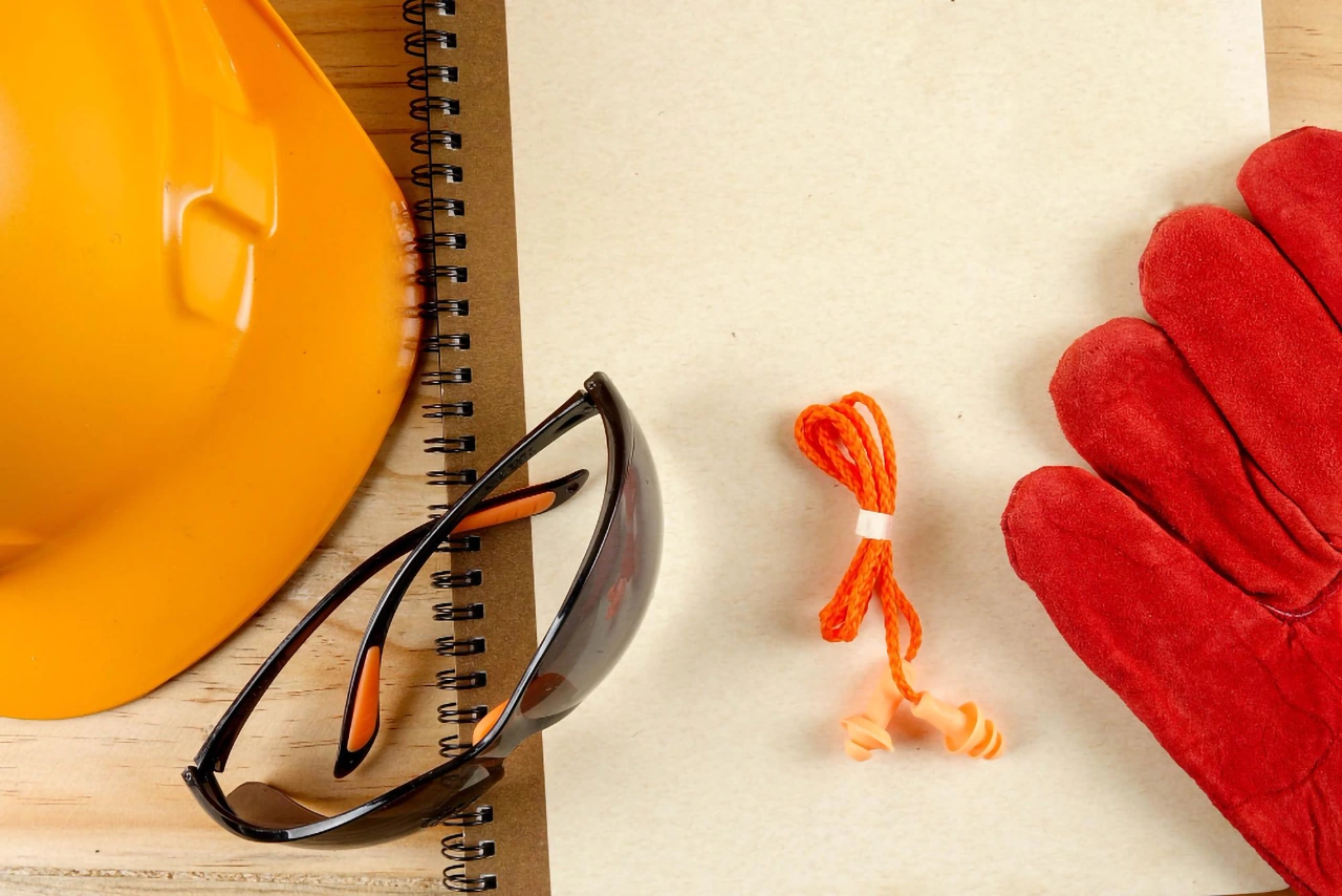 Safety gear including a hard hat, gloves, and sunglasses on notebook.