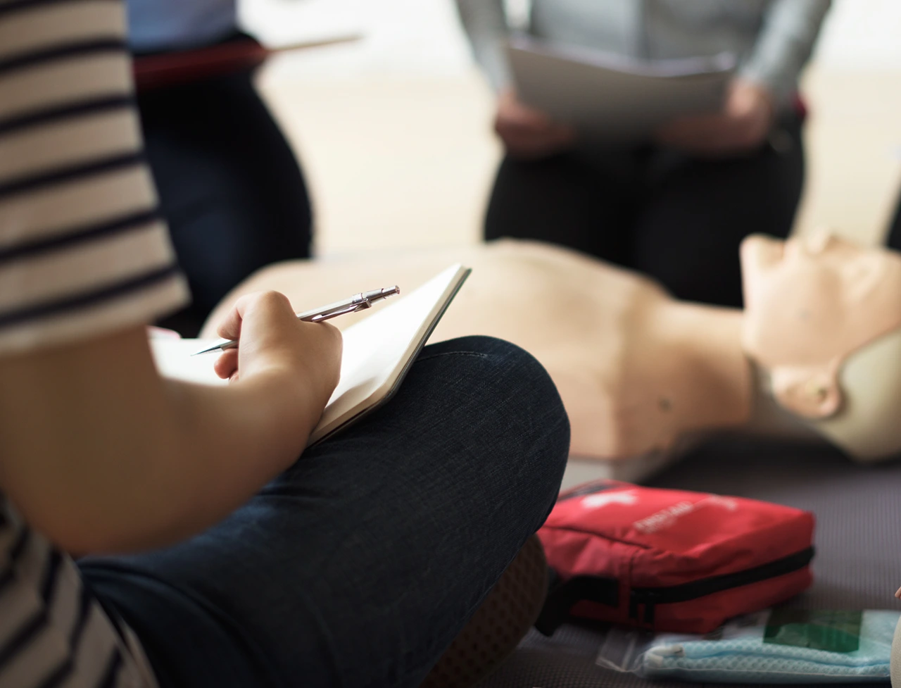 Participant taking notes during CPR training with a dummy.