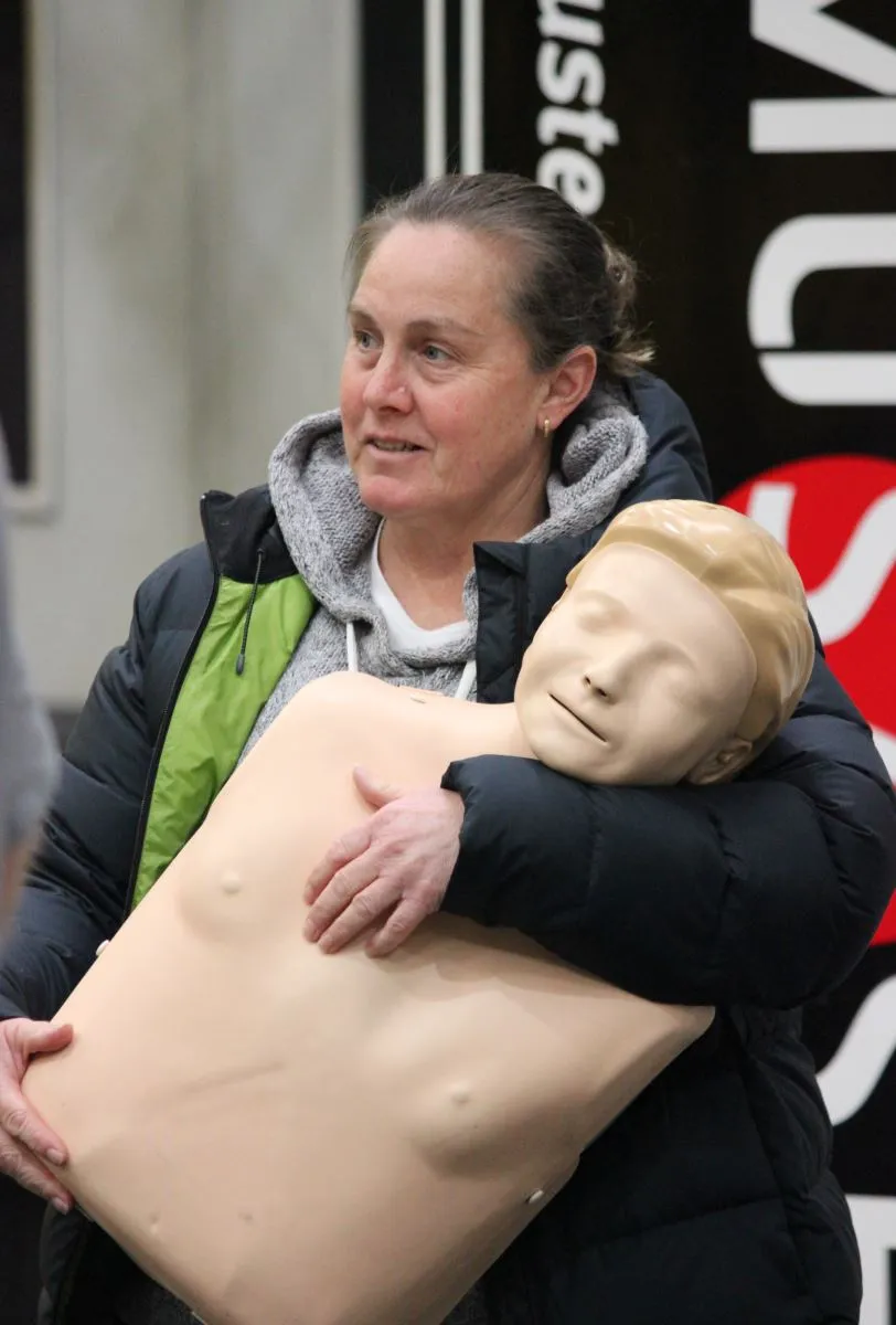 A woman holds a CPR training mannequin while smiling.
