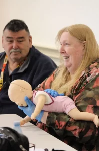 A woman demonstrating CPR techniques using a baby doll.