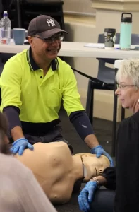 Man practicing CPR on a training mannequin in a classroom setting.
