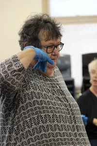 Woman with glasses and gloves gestures while listening attentively.
