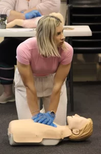 Instructor performing CPR on a training mannequin in class.