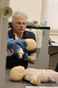 A man demonstrates infant CPR using a practice doll.