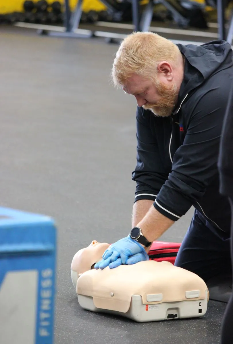 A person performing CPR on a training dummy in a gym setting.