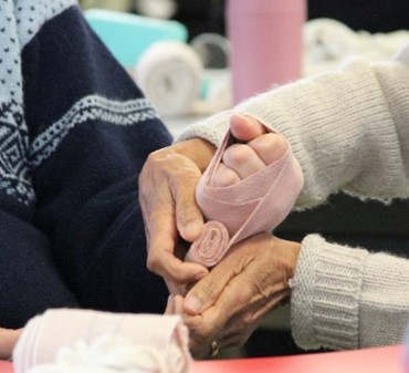 Hands applying a pink bandage to another person's arm.