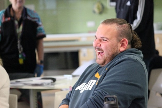 A man in a hoodie laughs joyfully while seated at a table.