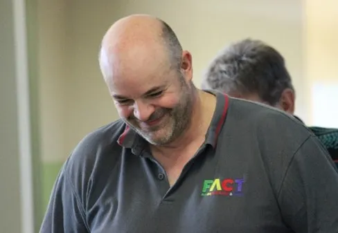 Smiling man wearing a gray shirt with color logo, indoors.