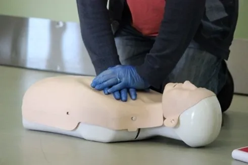 Practicing CPR on a medical training mannequin on the floor.