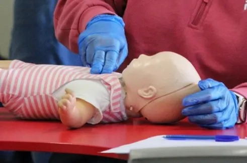 Adult demonstrating infant CPR on a training dummy.