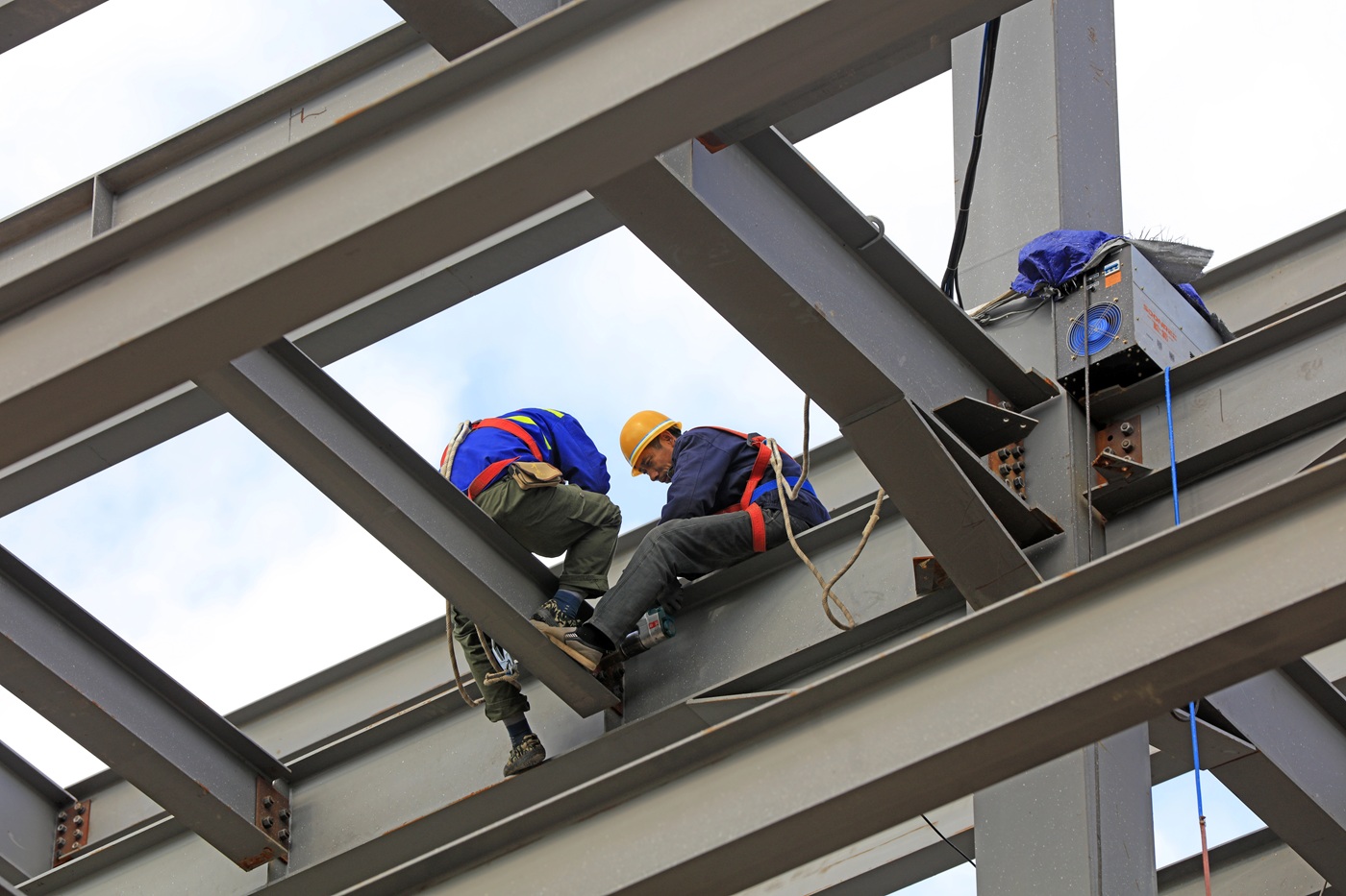 Two construction workers assembling a steel structure at height.